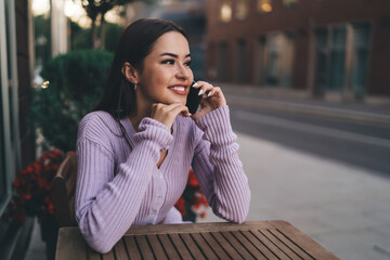 Content woman having phone conversation while sitting in city cafe