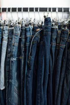 Vertical background image of blue denim jeans in row on clothing rack at thrift shop