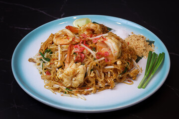A Plate of “Phad Thai” with prawn on table with green Chinese chive ground nuts with the black background . It’s a stir fried noodles which is a classic street food consider as national dish