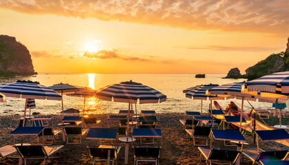 morning or evening landscape with nice beach with deck chairs and umbrellas during sunrise or sunset with amazing sea with rocks and beautiful clouds on background