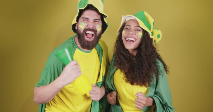 young couple soccer fans from brazil. cheering and cheering with flag and accessories.