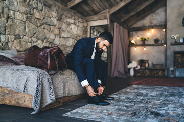 Confident man sitting on bed tying shoelaces