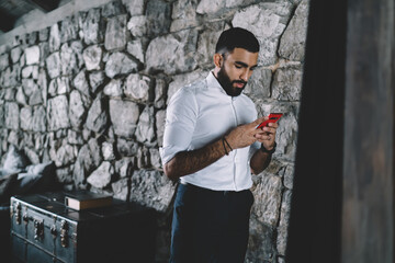 Ethnic man messaging on smartphone in modern apartment