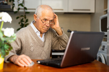 gray haired old man working at laptop at home