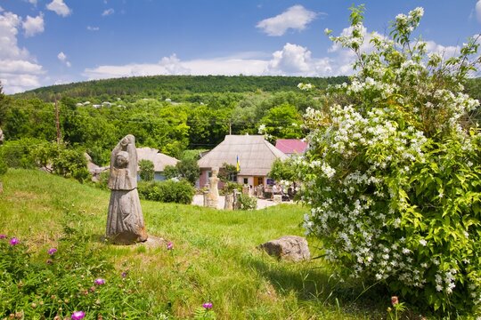 Busha, Ukraine - 09.06.2019: old town downtown, soviet time country house, Trypillya style neo pagan symbolic sculpture, blooming jasmine bush with tender white flowers, tourist sightseeing attraction