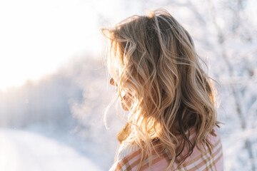 Young woman with blonde hair in winter clothes hands near face against background of snowy winter...