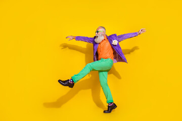 Fototapeta na wymiar Full length photo of positive funky man wear purple velvet jacket walking hands sides discotheque isolated yellow color background