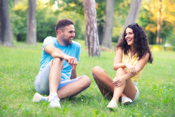 Young smiling couple sitting in the grass and talking on a sunny summer day