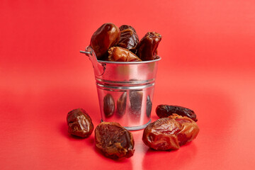 A small metal bucket filled with dried dates on a red background.
