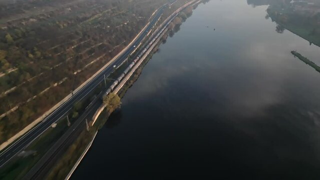 Train driving on railway along Elbe river and road near Melnik city in Czech Republic, drone following evening view