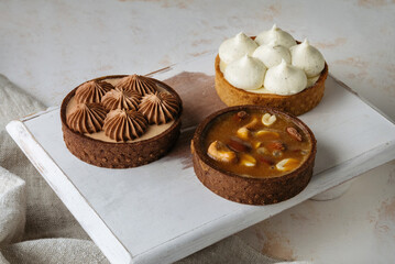 Mini chocolate cakes on wooden background. In the background is a cake with Cashew nut filling, almonds, peanuts.