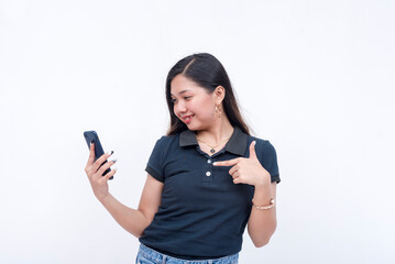 A young asian woman eagerly pointing to her phone. Wearing a dark blue polo shirt, khaki pants and...