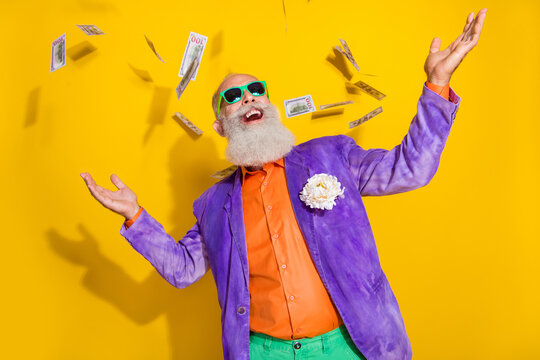 Photo of positive eccentric man granddad millionaire wear colorful bright costume rejoice usd banknotes isolated on yellow color background
