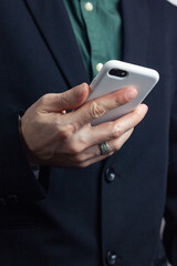 Male hands of a businessman in a business suit with a ring on his finger hold a modern gadget, a phone in a white case in his hands. Vertical orientation photo, business style.