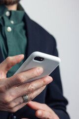 Male hands of a businessman in a business suit with a ring on his finger hold a modern gadget, a phone in a white case in his hands. Vertical orientation photo, business style.