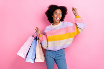 Photo of impressed ecstatic girl with perming coiffure knit sweater hold shopping bags clench fist isolated on pink color background