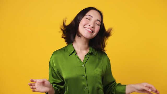 Beautiful fun fancy smiling happy young woman of Asian ethnicity 20s she wear green shirt dance waving fooling around have fun enjoy play fluttering hair isolated on plain yellow color wall background