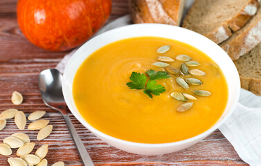 Healthy and tasty pumpkin cream soup and freshly bread on a wooden table. Close-up. Selective focus.