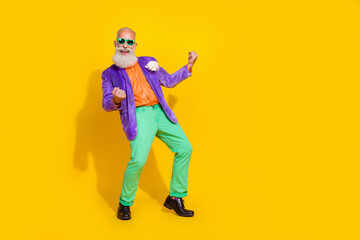 Full length photo of funky lucky man wear purple velvet jacket rising fists having fun discotheque empty space isolated yellow color background