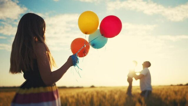 happy family celebrates birthday in the park. girl a holding colorful lifestyle balloons silhouette in the field. dad throws his son into the sky in the park. happy family kid dream concept
