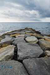Fototapeta na wymiar Rocks and stones on the coastline of Varazze, Liguria, Italy, with the rippled waters of mediterranean sea. Dramatic clouded sky on the background. Vertical view.