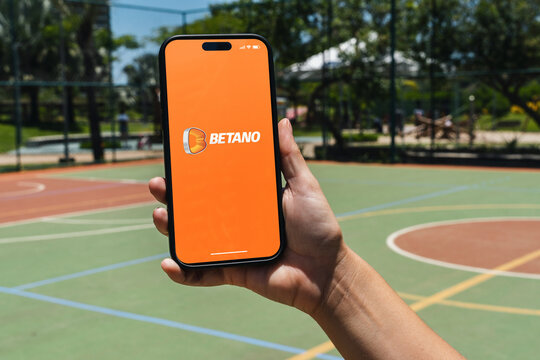 Girl holding an iPhone 14 Pro smartphone with Betano betting provider app on screen. Multi-sport court in the background. Rio de Janeiro, RJ, Brazil. November 2022