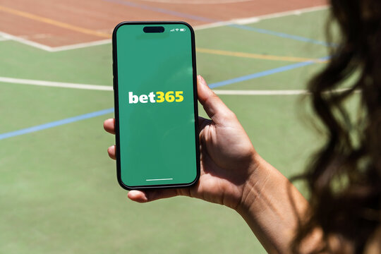 Girl holding an iPhone 14 Pro smartphone with Bet365 betting provider app on screen. Multi-sport court in the background. Rio de Janeiro, RJ, Brazil. November 2022