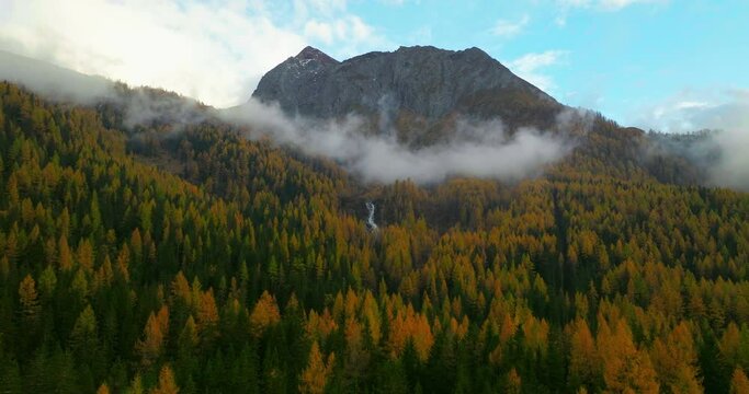 Casere mountain waterfall and low cloud passing across Autumn alpine forest trees, South Tyrol