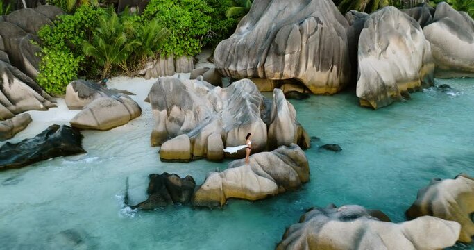 Aerial zoom out view Beautiful woman in a swimming costume standing on granite boulders at spectacular Anse Source d'Argent beach, La Digue,Seychelles