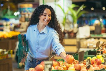 Happy woman buyer in supermarket, Latin American woman buys apples, fruits and vegetables, puts in...