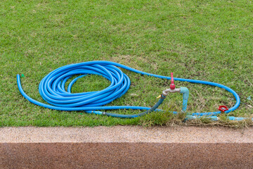 A blue plastic hose connected to a ready-to-open faucet valve is placed on the green lawn in a...