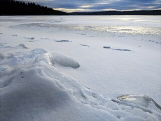 Ice covered in snow on the beach of a lake.