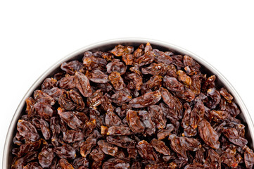 Dark-colored raisins lying in a metal container, shot on a white background.