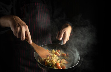 Cooking delicious food in a restaurant with fresh vegetables and pasta. The chef flips the food with a wooden spoon in a hot pan