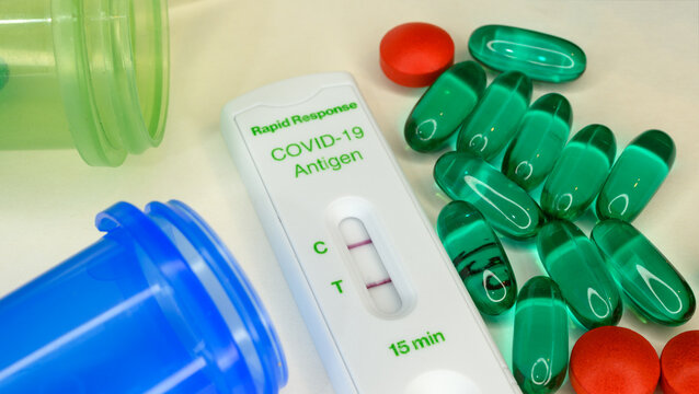 Closeup Of A Positive COVID-19 Antigen Test With Two Pill Bottles And Scattered Generic Acetaminophen And Ibuprofen Medication.
