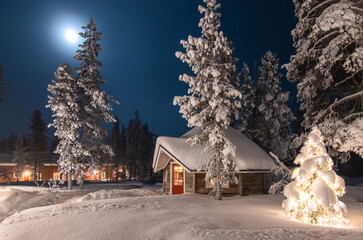 Outdoor winter and Christmas scene with wooden cabin in the woods. Winter forest landscape at full moon, Finland, Lapland. 