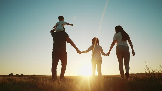 people in the park. happy family walking silhouette at sunset. mom dad and daughters walk holding hands in the park. happy family sun childhood dream concept. parents and children go back silhouette