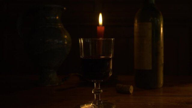 Verre de cristal contenant du vin rouge &agrave; la lueur d'une bougie et bouteille de vin (mouvement arri&egrave;re)