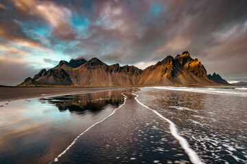 Sunlight on Vestrahorn, Stokksnes peninsula. Golden hour shot with reflection at dusk and leading line ripples on the black sand beach