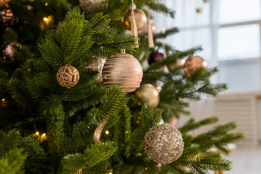 Golden Christmas balls hanging on fir tree against blurred festive lights. winter Holiday background. Festive and cozy. Happy new year