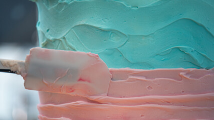 cake designer covering a frosted blank cake with turquoise light blue and pink cream with spatula - obrazy, fototapety, plakaty