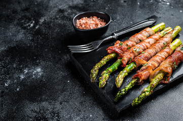 Asparagus Baked with bacon and spices. Black background. Top view. Copy space