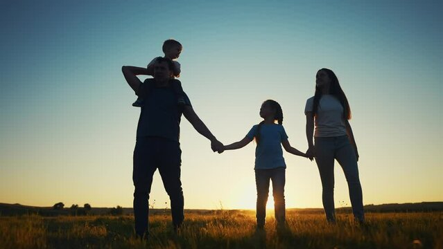 people in the park. happy family walking silhouette at sunset. mom dad and daughters walk holding hands in sun the park. happy family childhood dream concept. parents and children go back silhouette