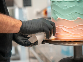 cake designer covering a frosted blank cake with turquoise light blue and pink cream with spatula