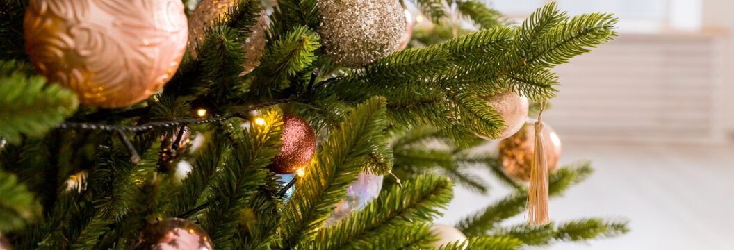 Gold Christmas ball on a Christmas tree in a light interior against the background of burning garlands of lights. Decorating Christmas tree Happy holidays. Web banner