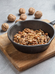 Roasted walnuts in black pan and walnut shells against concrete background. Close up.