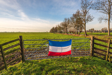 Inverted Dutch flag mounted on a gate in front of a muddy meadow in the Alblasserwaard region. This...