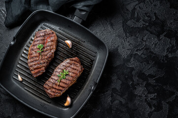 Grilled Top Blade or flat iron roast beef meat steaks on a skillet. Black background. Top View....