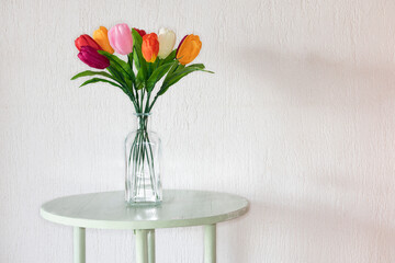 Botella de vidrio  con tulipanes de colores, sobre una mesa y cerca de la pared blanca, luz natural de la ventana