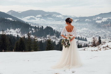 Bride in white wedding dress holding colorful flowers bouquet in hands and posing outdoors. Winter wedding and season floral concept. Mountains on background.
- 548000158